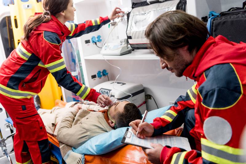Two EMTs in uniforms provide medical care to a patient inside an ambulance