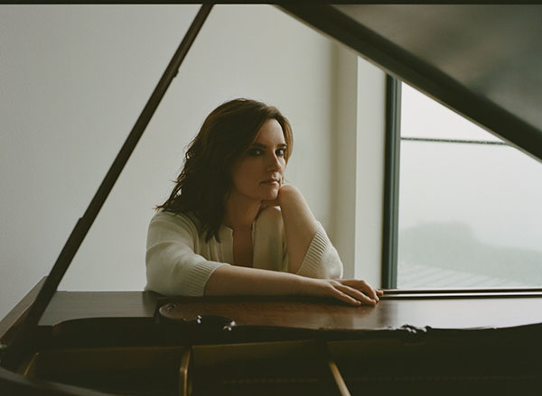 Brandy Clark is pictured in a white sweater sitting at a piano